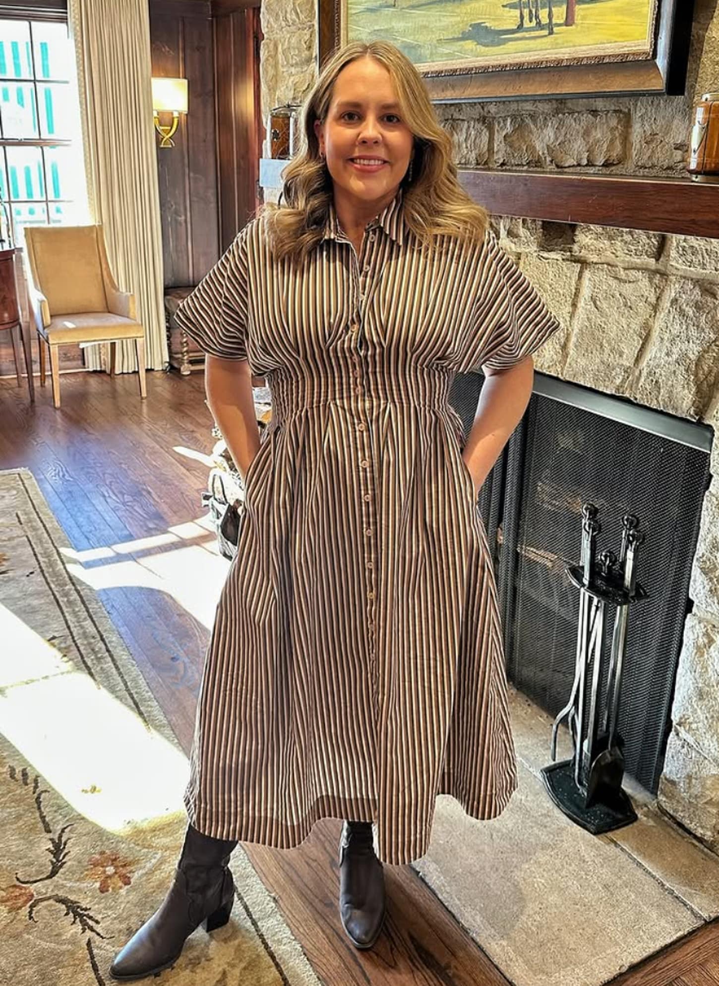 Kate Wiewel in home standing near the fireplace in a dress and boots
